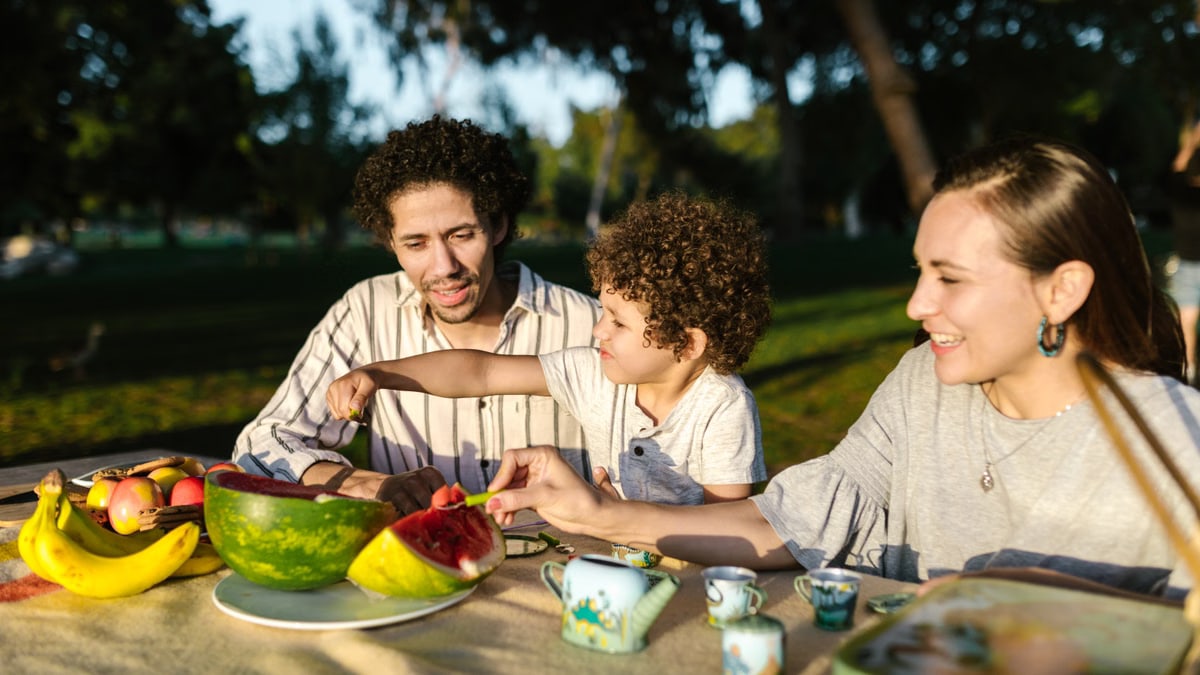 Happy family having a joyful picnic with fruits and snacks in a park during summer.